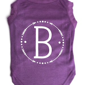 May include: Purple dog shirt with a white circle design featuring the letter "B" and arrows.