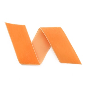 K&ouml;nnte beinhalten: Ein leuchtend orangefarbenes Samtband ist zu einer dekorativen Form gedreht und gefaltet.