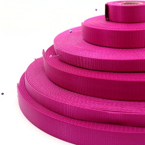 May include: A stack of four pink nylon webbing straps of different widths. The straps are arranged in a pyramid shape with the widest strap at the bottom and the narrowest strap at the top.