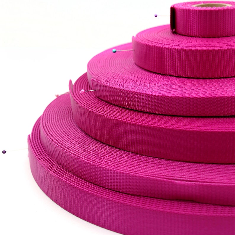 May include: A stack of four pink nylon webbing straps of different widths. The straps are arranged in a pyramid shape with the widest strap at the bottom and the narrowest strap at the top.