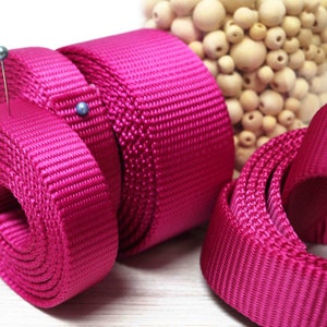 May include: Close-up of pink nylon webbing rolled up. The webbing is textured and has a shiny finish.