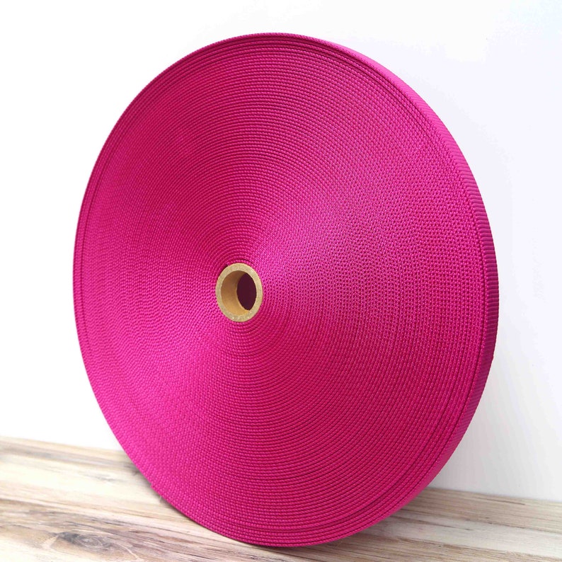 May include: A roll of bright pink nylon webbing, a type of strong, durable fabric often used for straps, belts, and other applications.