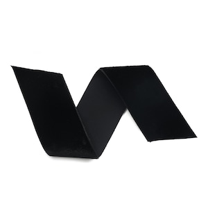 Op de afbeelding: Een zwart fluwelen lint, gevouwen in een zigzagpatroon, geïsoleerd op een witte achtergrond.