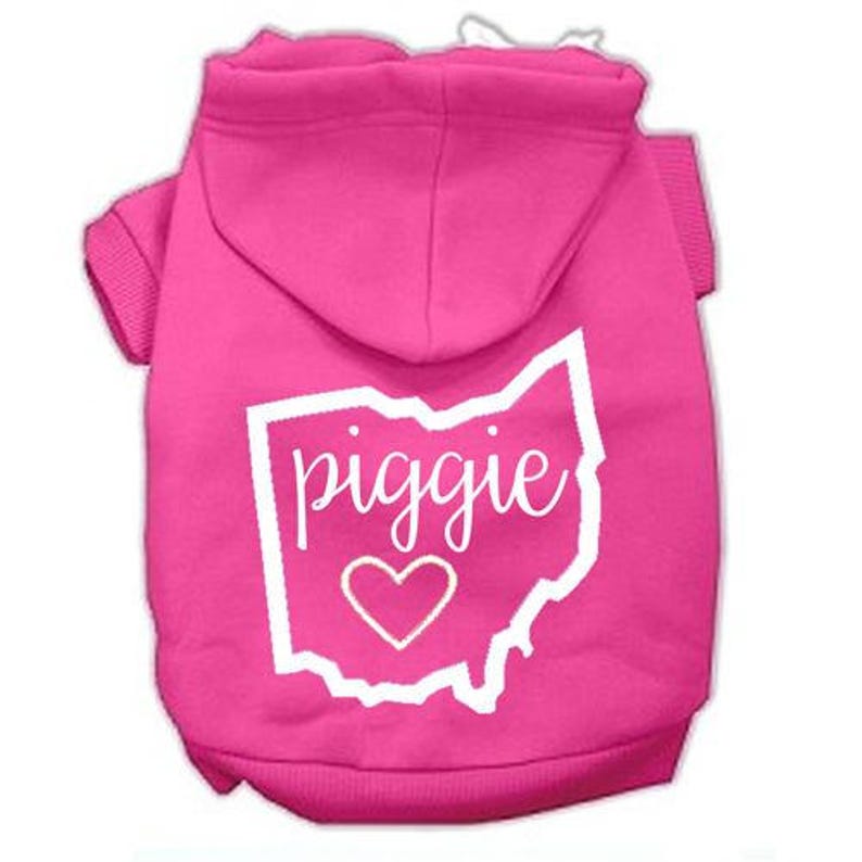 Puede incluir: Sudadera rosa para perro con un contorno blanco del estado de Ohio y la palabra "piggie" en su interior. Un peque&ntilde;o coraz&oacute;n blanco est&aacute; dentro del contorno.
