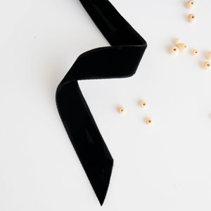 May include: A black velvet ribbon on a white background with scattered wooden beads.