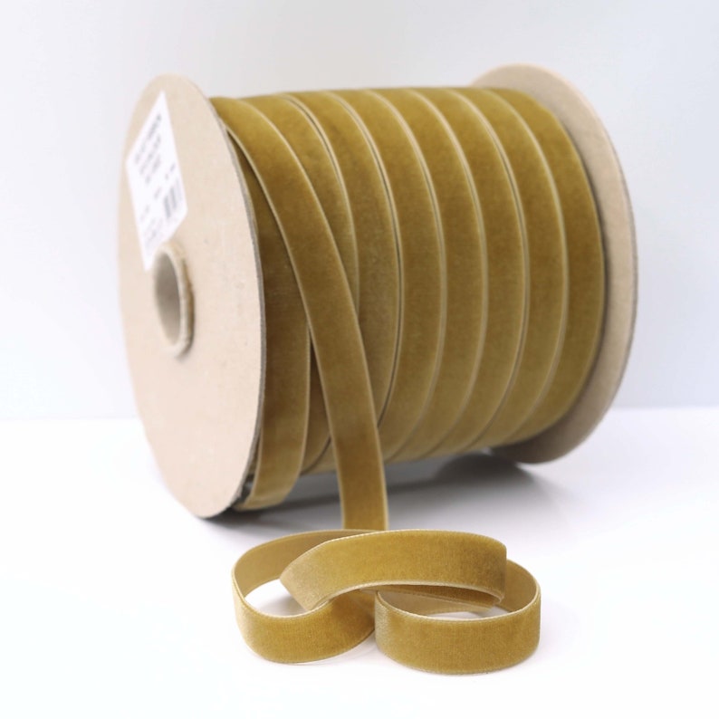 May include: A spool of gold velvet ribbon. The ribbon is approximately 1/2 inch wide and is wound around a cardboard spool.