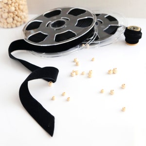 May include: A spool of black velvet ribbon with wooden beads scattered around it.