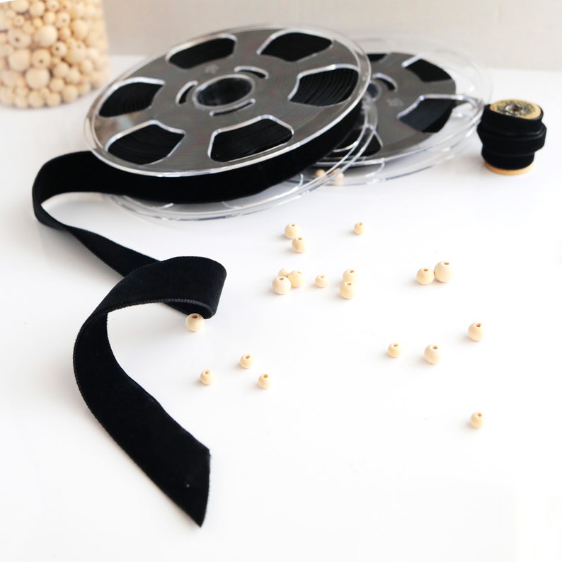 May include: A spool of black velvet ribbon with wooden beads scattered around it.