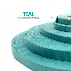 May include: Close-up of teal heavy-duty nylon webbing rolls. The rolls are stacked, showing different widths of the material. The word "TEAL" is printed above the webbing, with the text "Heavy Duty Nylon Webbing" below it. Pins are inserted into the webbing.