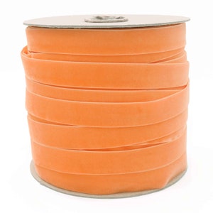 K&ouml;nnte beinhalten: Eine Spule mit leuchtend orangefarbenem Samtband. Das Band ist fest auf eine Pappspule gewickelt.