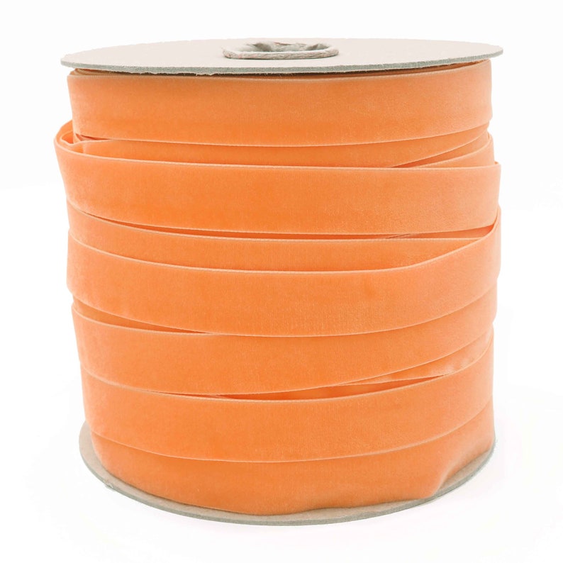 K&ouml;nnte beinhalten: Eine Spule mit leuchtend orangefarbenem Samtband. Das Band ist fest auf eine Pappspule gewickelt.