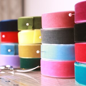 Peut inclure: Une pile de bobines de ruban de velours de diff&eacute;rentes couleurs, chacune avec une &eacute;pingle au centre. Les rubans sont de couleurs vari&eacute;es, notamment rouge, jaune, bleu, vert et rose.