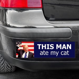May include: A black car with a bumper sticker that says "THIS MAN ate my cat". The sticker features a photo of a man with a red, white, and blue American flag in the background.