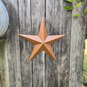 May include: A large, five-pointed star made of metal with a rustic, copper finish. The star is mounted on a weathered wooden surface.
