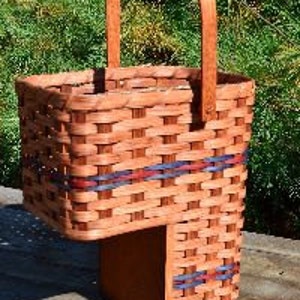 May include: A woven basket with a handle, featuring a red, white, and blue striped design. The basket has a unique stepped shape, with a smaller section extending out from the bottom.