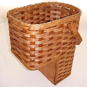 May include: A brown wicker basket with a wooden base and a handle. The basket is woven with a tight, even pattern.