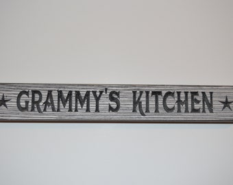 May include: A wooden sign with the text "GRAMMY'S KITCHEN" in black lettering with a star on each side.
