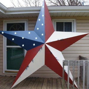 May include: A large, red, white, and blue star-shaped metal sign with a distressed paint finish. The star is hanging on the side of a house.