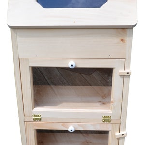 May include: A wooden cabinet with two shelves and glass doors. The cabinet has a hinged top with a glass window. The cabinet is made of light wood and has brass hinges.
