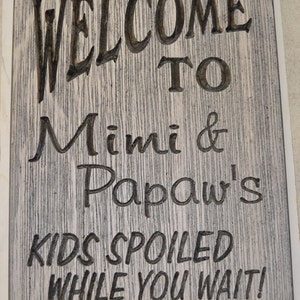 May include: A wooden sign with the text "Welcome to Mimi & Papaw's Kids Spoiled While You Wait!" in black lettering on a whitewashed wood background.