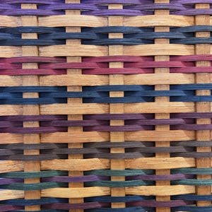 May include: A woven basket with a pattern of brown, purple, green, and blue stripes. The basket is made of natural materials and has a rustic look.
