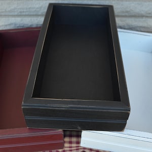 May include: Three wooden trays in different colors: burgundy, black, and white. The trays are rectangular and have a simple, rustic design.