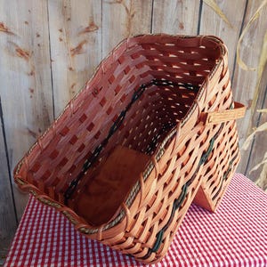 May include: A large, woven basket with a brown and green pattern. The basket has a handle and is made of natural materials.