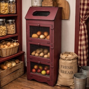 May include: A burgundy wooden storage cabinet with wire mesh doors, filled with produce. A burlap sack with "FRESH BREAD" is next to the cabinet. Jars of food and a wooden sign that says "BREAD" are also visible.