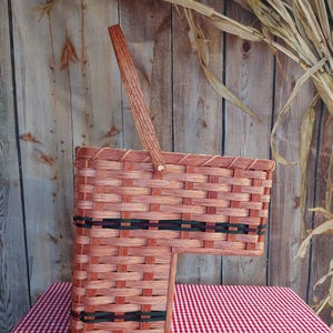 May include: A brown wicker basket with a wooden handle and black and green trim. The basket is sitting on a red and white checkered tablecloth.