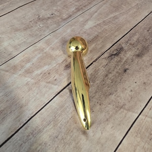 May include: A gold-colored metal hook with a rounded top and a curved, pointed bottom. The hook is designed for hanging items.