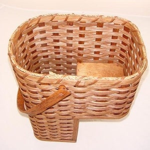May include: A woven wicker basket with a wooden base and a wooden handle. The basket is brown and has a natural finish.