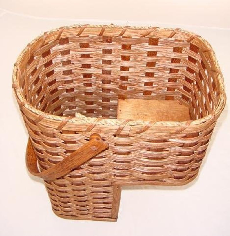 May include: A woven wicker basket with a wooden base and a wooden handle. The basket is brown and has a natural finish.