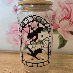 May include: A clear glass jar with a bamboo lid features a black silhouette of two dragons flying through a geometric archway with stars and dice.