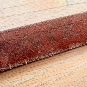 May include: Close-up of a brown leather belt with the word "STIX" embossed on the surface.