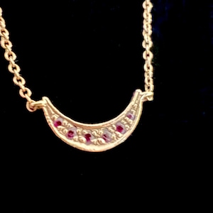 May include: A gold crescent moon necklace with small red gemstones set into the crescent shape.