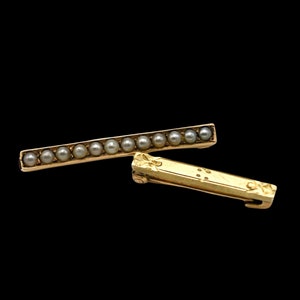 May include: A gold bar brooch with a row of pearls. The brooch has a decorative clasp.