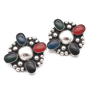 May include: A pair of silver earrings with a flower design. Each earring has five stones in different colors: green, blue, red, and black.
