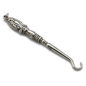 May include: A silver shoe horn with an ornate, detailed handle. The handle is decorated with a floral design.