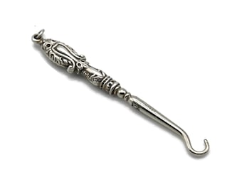 May include: A silver shoe horn with an ornate, detailed handle. The handle is decorated with a floral design.