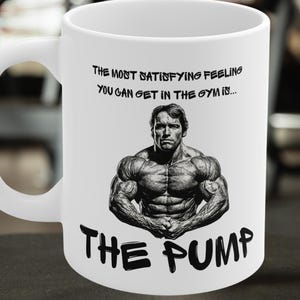 May include: White ceramic mug featuring a black and white image of a bodybuilder and the text "The most satisfying feeling you can get in the gym is... The Pump."