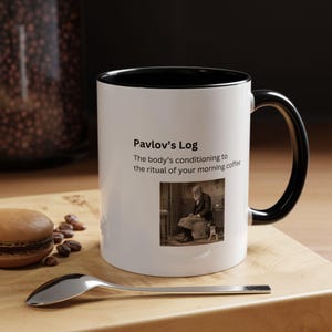 Puede incluir: Taza de café blanca con borde y asa negros. La taza presenta una imagen en blanco y negro de Iván Pávlov y un perro, con el texto "Pavlov's Log: The body's conditioning to the ritual of your morning coffee."