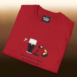Pode incluir: Camiseta vermelha com um gráfico engraçado com uma caneca de cerveja escura, um aspirador e um tucano. O texto "After reviewing the evidence, the 'G' has been split!" está impresso abaixo. A camisa tem uma etiqueta que diz "WILBER GAMES".