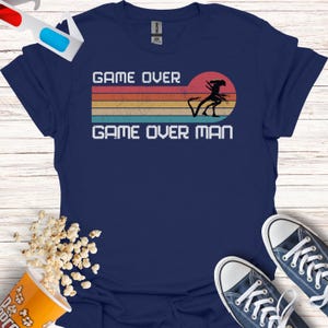 May include: A navy blue t-shirt with a retro-style graphic of an alien with the text "Game Over Man" in white.