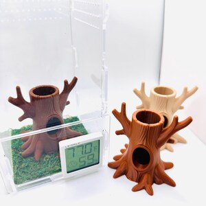 May include: Three brown tree stump decorations with a hollow center and branch-like protrusions. One stump is inside a clear plastic terrarium with a digital thermometer displaying 77.0°F and 59%. The other two stumps are tan and brown.