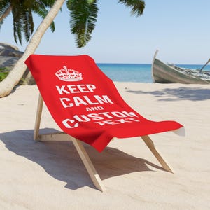 May include: Red beach towel with a white crown and the text "Keep Calm and CUSTOM TEXT" on a wooden beach chair on a sandy beach.