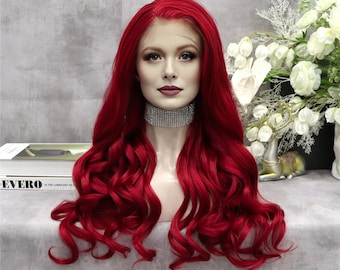 Puede incluir: Una peluca roja vibrante con mechones largos y ondulados. La peluca se muestra en una cabeza de maniquí, mostrando su rico color y textura. El maniquí lleva un collar de diamantes de imitación plateado. El fondo incluye un arreglo floral y un libro.
