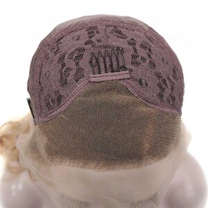 May include: Close-up of a wig cap, showcasing the lace front and the intricate lace pattern on the crown. The cap is a muted mauve color, with a fine mesh and small combs for secure attachment. The wig's base is visible.