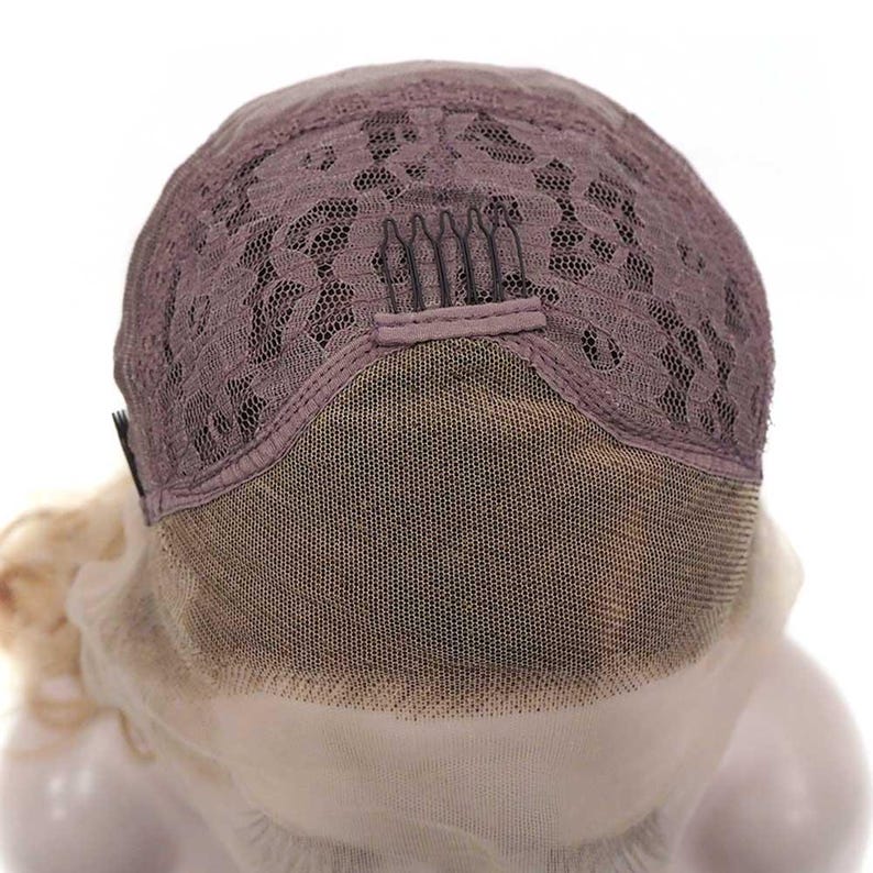 May include: Close-up of a wig cap, showcasing the lace front and the intricate lace pattern on the crown. The cap is a muted mauve color, with a fine mesh and small combs for secure attachment. The wig's base is visible.