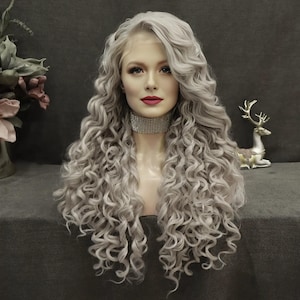 May include: A long, wavy, silver-grey wig with a lace front. The wig features voluminous, tightly curled locks. The mannequin head is adorned with a sparkling choker. The background is a muted grey.