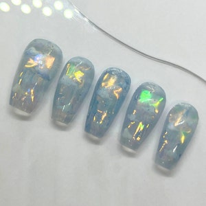 Puede incluir: Conjunto de seis uñas postizas iridiscentes azules y blancas con un diseño de nubes.